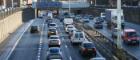 Cars going in both directions on a motorway with tall sides and signs overhead 