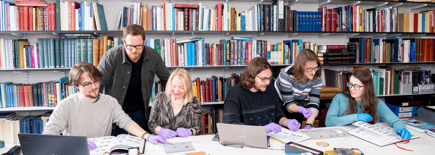 Students studying coins in library wearing purple gloves