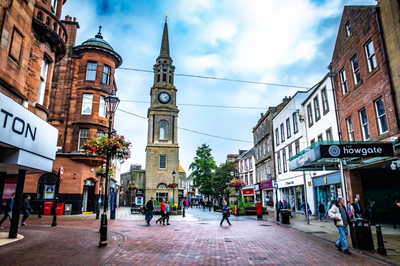 Image features the centre of Falkirk Highstreet including a series of shops and a church