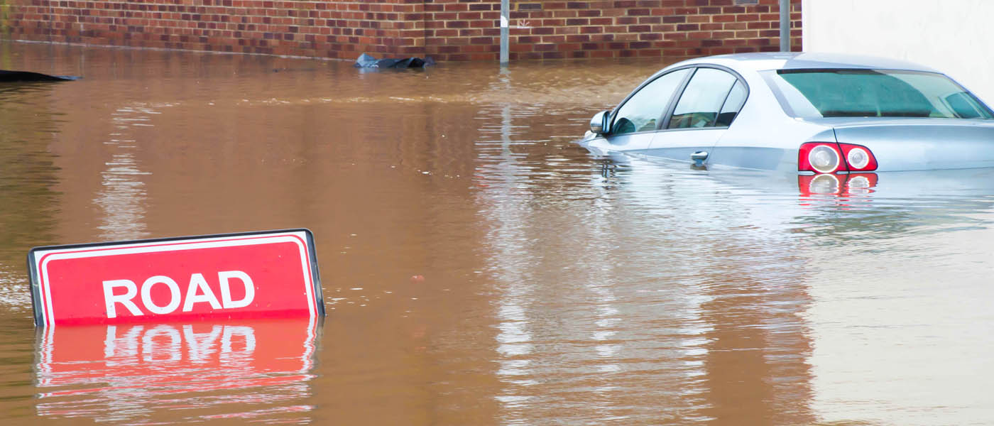 Road closed sign because of flooding with a car partly submerged in the flood water.