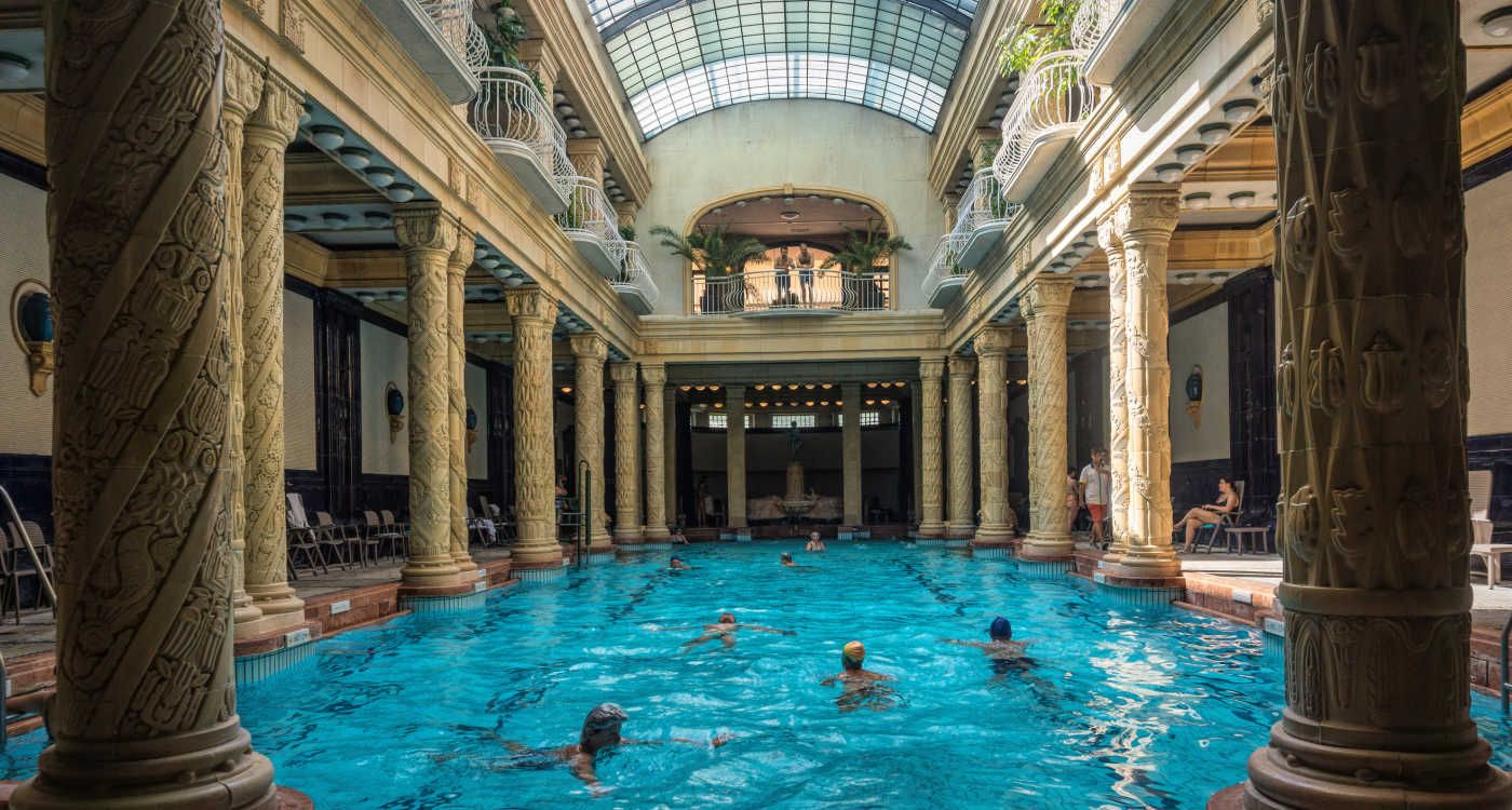 Pool inside St Gellert thermal bath showing people swimming in the waters under a glass dome ceiling [Photo: Shutterstock]