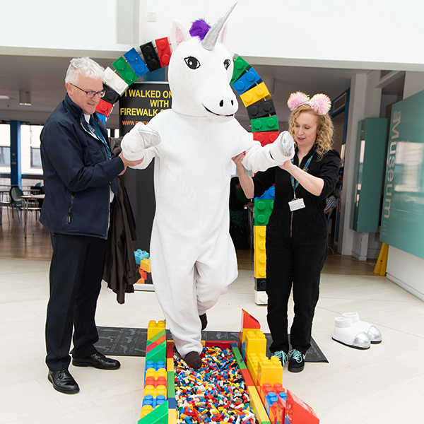 Staff members helping Cornelius the unicorn along the LEGO walk