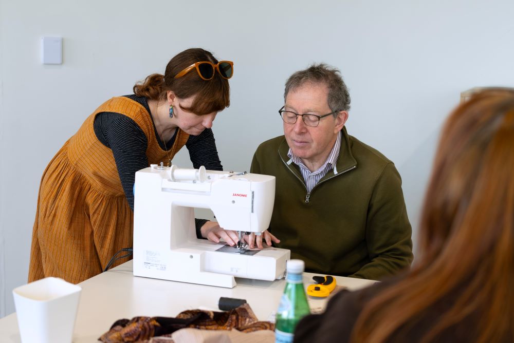 A woman assists a man using a sewing machine