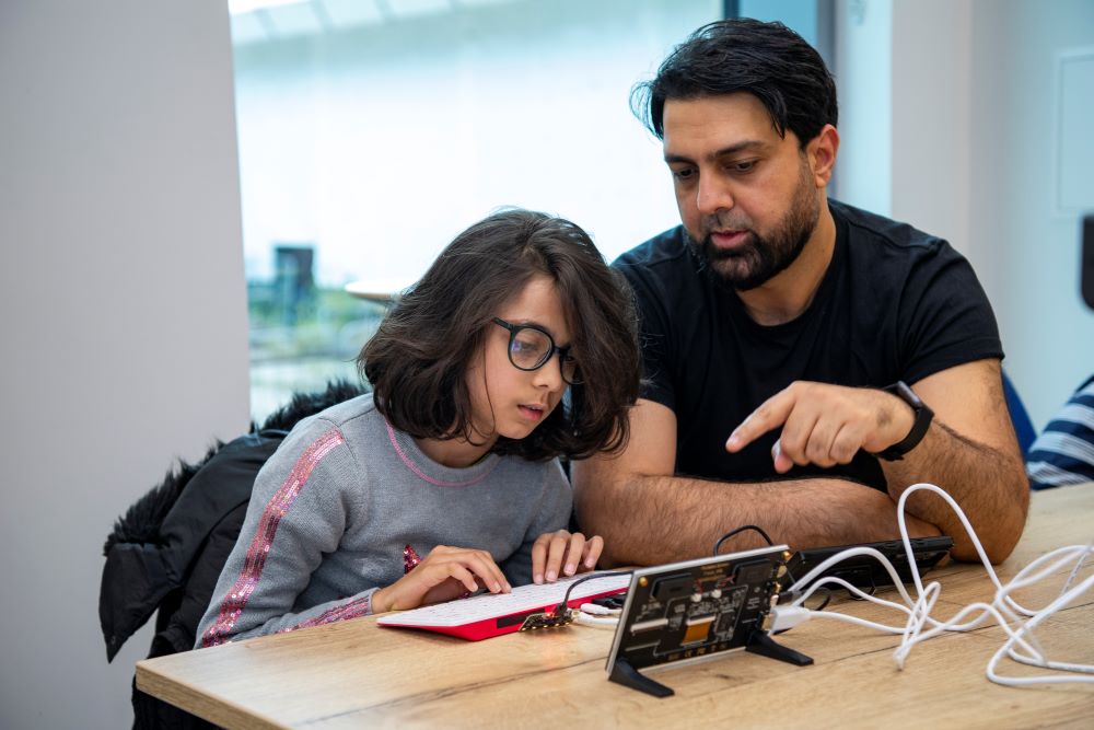 A man assists a young person to code an electronic device