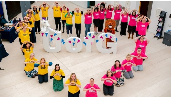 Volunteers in pink and yellow tshirts standing in a heart shape