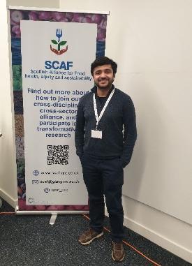 Picture of Dr Santosh Gaihre standing in front of the SCAF banner