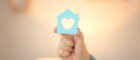 A two-dimensional blue house with a heart cutout in the centre, held by a hand