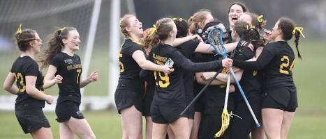 Glasgow University Lacrosse team celebrating on grass. Goal in background and all in black strips