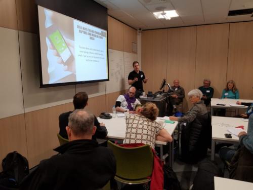 photo of teaching setting: a middle-aged white man in shirt gesticulating while teaching an older audience