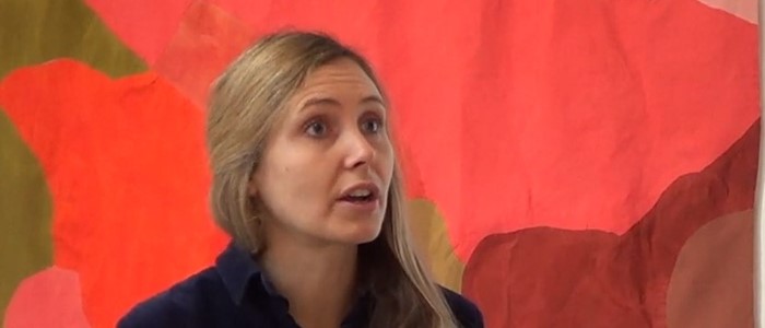 bust shot of a young white woman with long blond hair in front of a red background