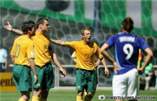 photo of 4 white men in footballer's attire, with the 2 in the middle pointing left with their arm extended. Shoulder of the second man is hidden behind the first, so the third man looks like he has an unnaturally long arm composed of his own shoulder and forearm plus the team-mate's forearm. 