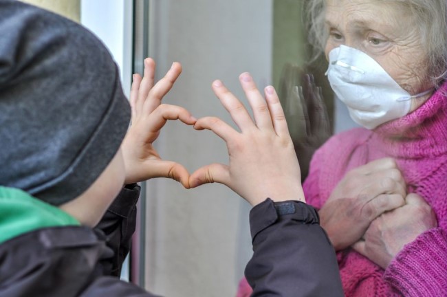 Eldery lady shielding from COVID with grandchild through a window