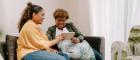 Two women, one young and one older, are stitting on a sofa and smiling as they look at tablet computer. Source: Centre for Aging Better Library https://ageingbetter.resourcespace.com/pages/view.php?ref=10527&k