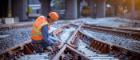 Rail worker wearing a high visibility jacket while on a train track working and fixing the lines. There's also a yellow stationary train on the track in the distance Source: DSCimage Publisher: Istockphoto Link: https://www.istockphoto.com/photo/portrait-engineer-under-inspection-and-checking-construction-process-railway-switch-gm1269800276-372989824