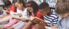 A group of children sitting on the floor and reading multiple different books with a bookshelf behind them. Source wavebreakmedia Publisher: istockphoto Link: https://www.istockphoto.com/photo/school-kids-sitting-on-cushions-and-studying-over-books-in-a-library-gm1138365810-303881460?clarity=false