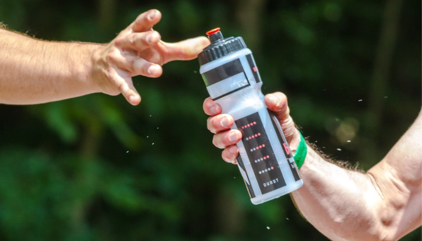 Two mens arms, one passing a plastic water bottle to the other. 