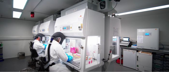 People wearing air-tight suits in a high containment facility conducting research in fume hoods. 